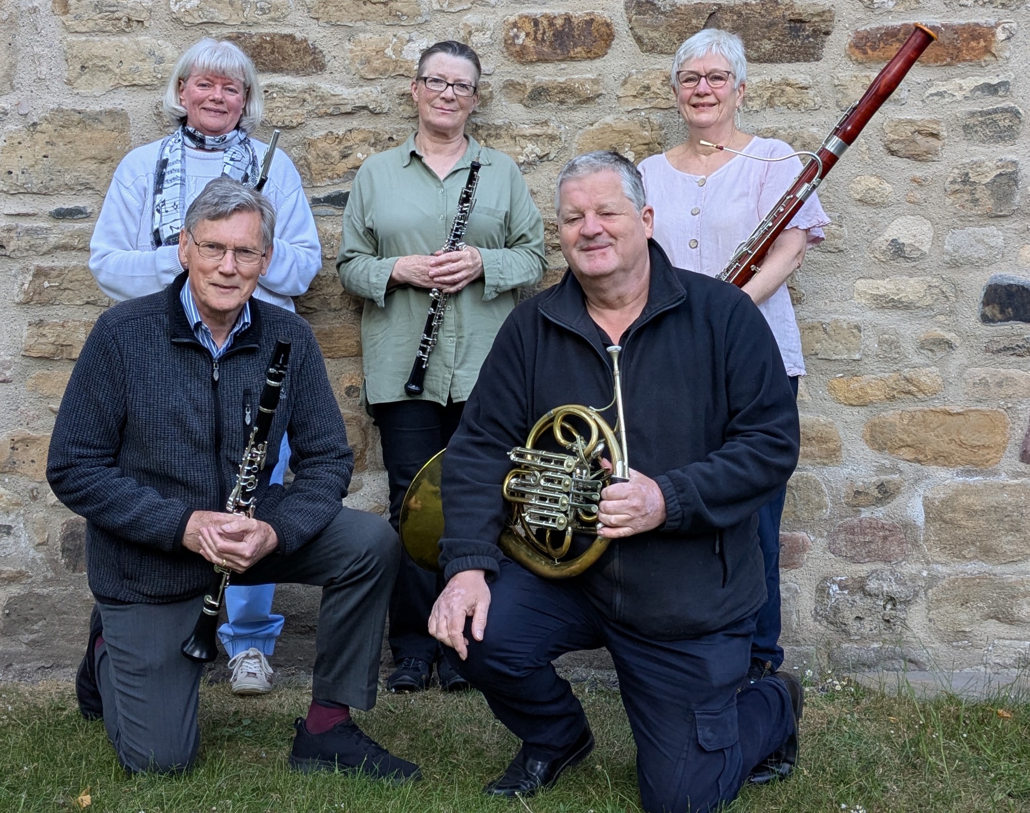 The five members of the Boreal Wind Quintet with their flute, oboe, clarinet, horn and bassoon, in front of a stone wall